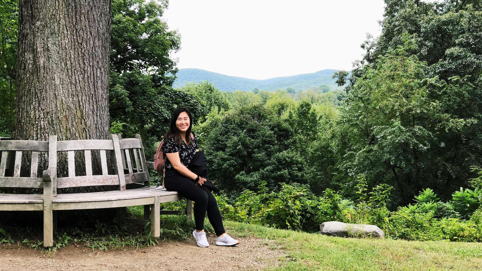Emily Chu is sitting on a. bench, surrounded by trees.